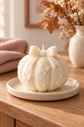 White butterfly bow pumpkin candle on a ceramic tray in a warm autumn home setting.