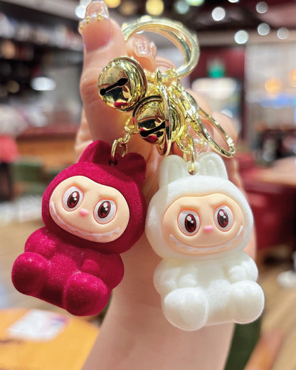 Two labubu keychains, one pink and one white, held in a hand with a blurred restaurant background.